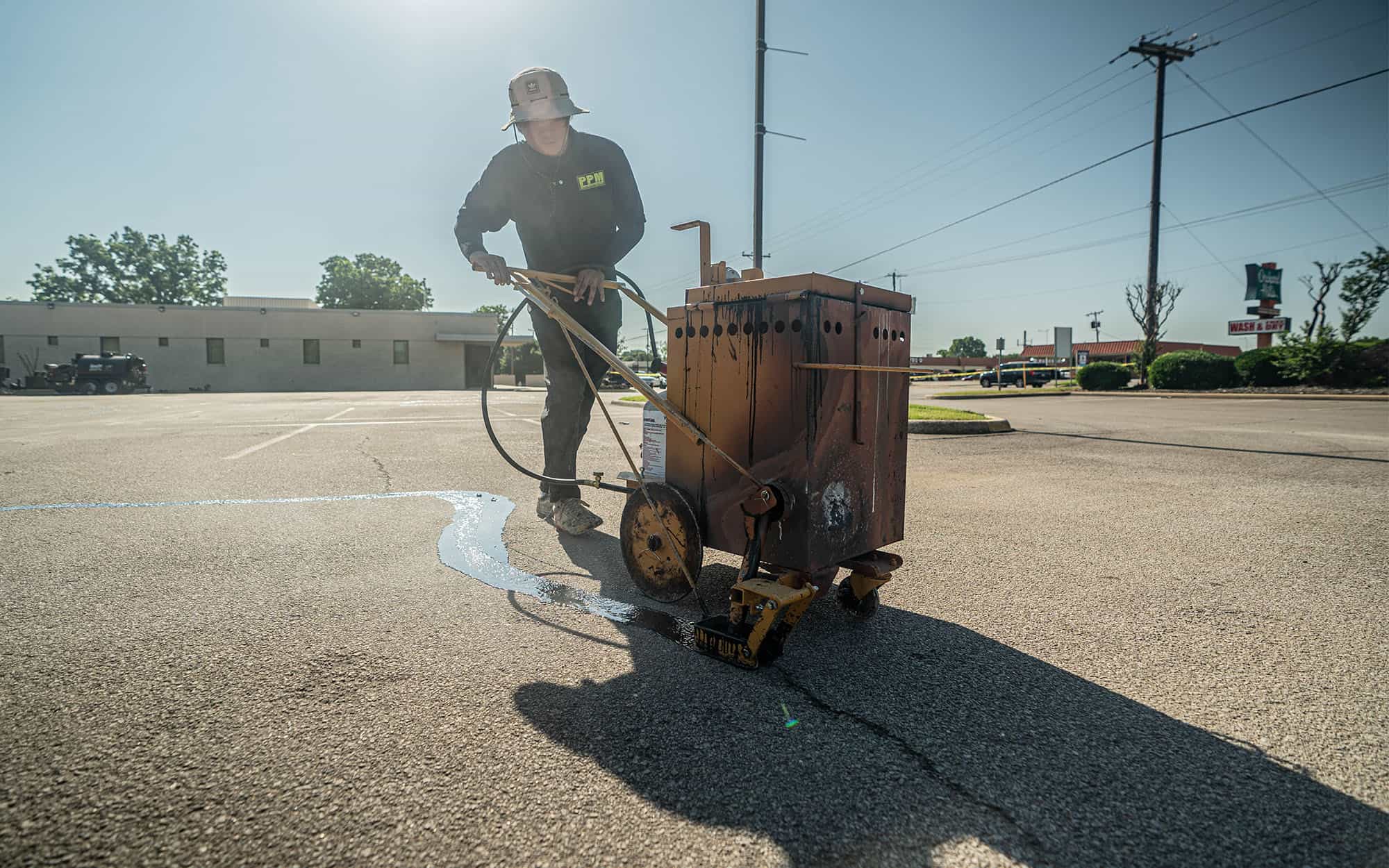 Man pushing machine that fills in parking lot cracks