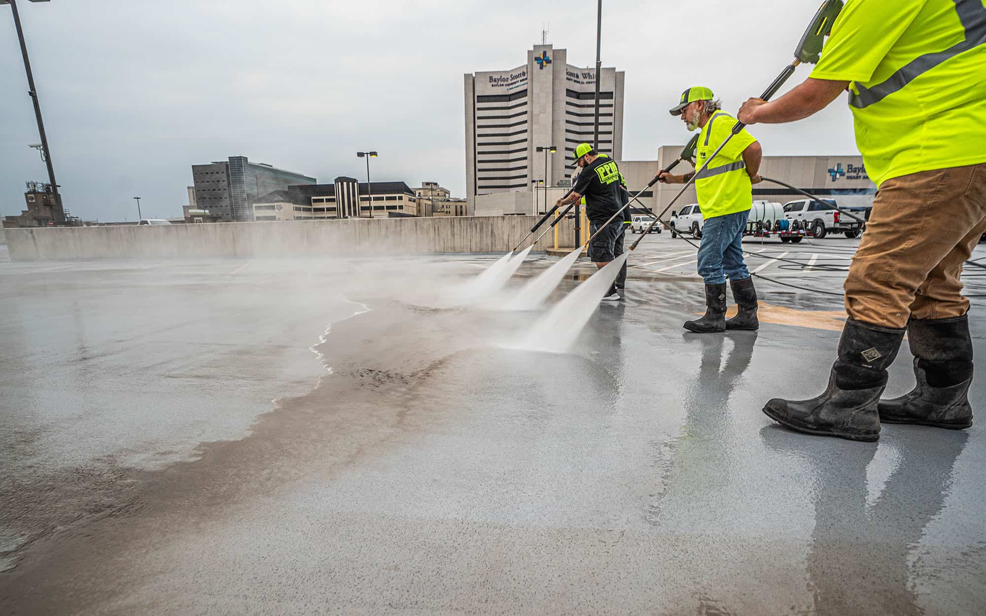 Side view of four PPM employees powerwashing the top level of a hospital parking garage